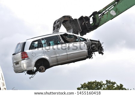 Car in a scrap yard being lifted by a mechanical grabber crane to be scrapped 