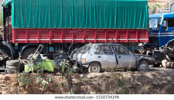 Car scrap yard on Madagascar, small car in front of\
a truck