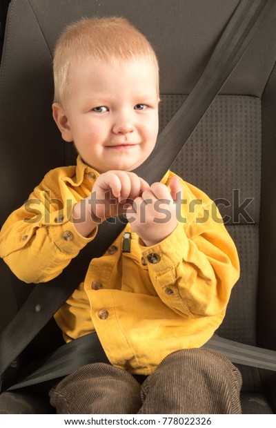 Car seat belt. A happy\
child is sitting in auto armchair next to a toy bear. The concept\
of road safety.