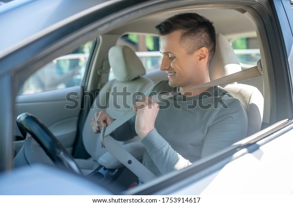 Car, seat belt. Interested\
man sitting in the driver\'s seat of a car, smiling with his seat\
belt on.