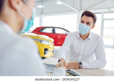 Car Seller And Customer Sitting At The Table In Car Salon And Shaking Hands Because They Got A Deal. Corona Virus.