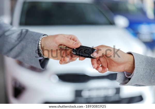 Car seller handing car keys to a customer while\
standing in car salon.