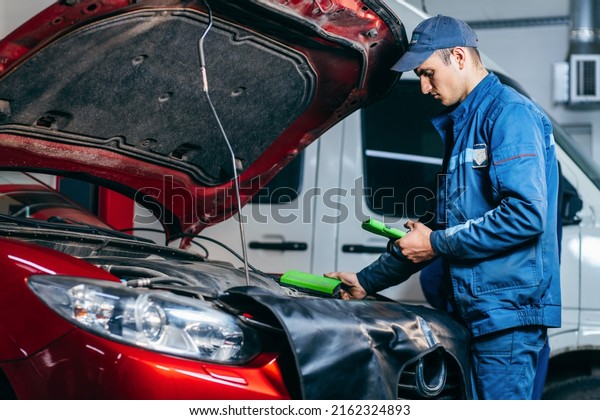 Car service electrician or mechanic uses a tablet
computer with futuristic interactive diagnostics software.
Inspecting the vehicle in order to find broken components in the
engine bay of modern car