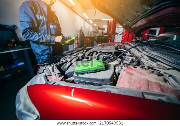 Car service electrician or mechanic uses a tablet\
computer with futuristic interactive diagnostics software.\
Inspecting the vehicle in order to find broken components in the\
engine bay of modern car
