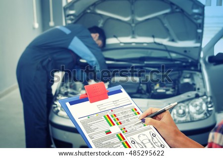 Car service. Holding the check list while car mechanic fixing the car in the background. Maintenance. Car broken down. Car break down. Car broke.