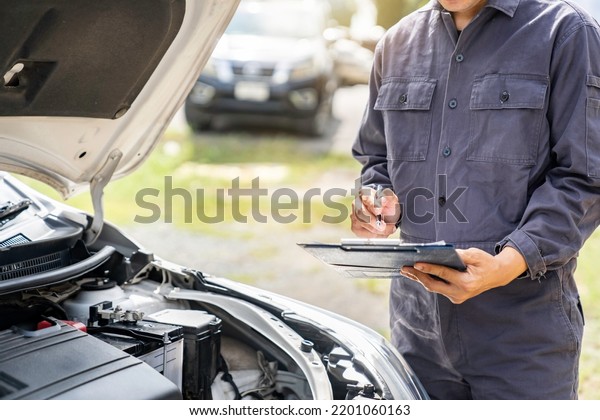 car service and maintenance. Services car engine\
machine concept, Automobile mechanic repairman checking a car\
engine with inspecting writing to the clipboard the checklist for\
repair machine