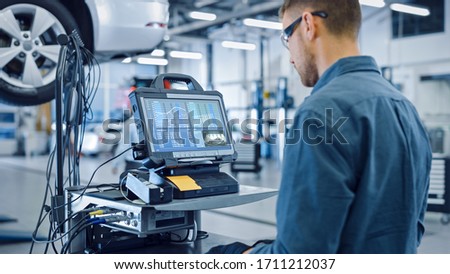 Car Service Manager or Mechanic is Running an Interactive Diagnostics Software on an Advanced Computer. Specialist Inspecting the Vehicle in Order to Find Broken Components and Errors in Data Logs.