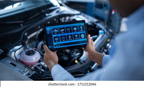 Car Service Manager or Mechanic Uses a Tablet Computer with a Futuristic Interactive Diagnostics Software. Specialist Inspecting the Vehicle in Order to Find Broken Components In the Engine Bay. - Powered by Shutterstock