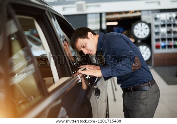 Car service manager sweeps\
his hand across the hood of a car and check the painting in the\
sunlight.