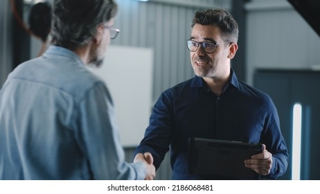 In a car service a manager with a tablet greeting a male with hand shakes, client talking to him and consulting about repairing a car - Powered by Shutterstock