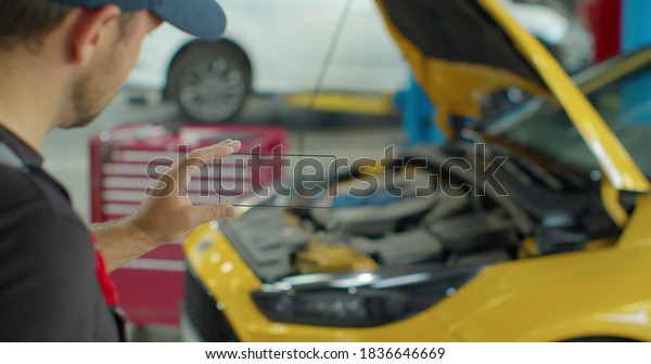 Car Service Manager Uses a smartphone\
transparent hologram digital display application in a car service.\
Professional car mechanic is working with diagnostics gadget on a\
vehicle in a service.