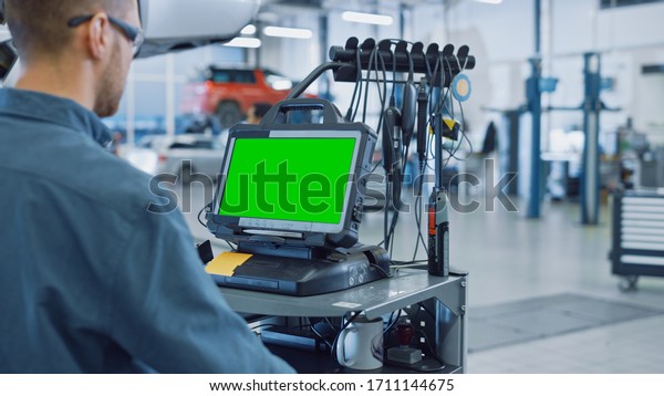Car Service Mechanic is Running a Diagnostics\
Software on an Advanced Computer with Green Screen. Specialist\
Inspecting the Vehicle in Order to Find Broken Components and\
Errors in Data Logs.