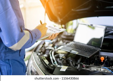 Car Service, Repair, Maintenance  Concept - Auto Mechanic Man Or Smith Writing To The Clipboard At Warehouse Workshop, Technician Doing The Checklist For Repairs Engine A Car In The Garage With Laptop