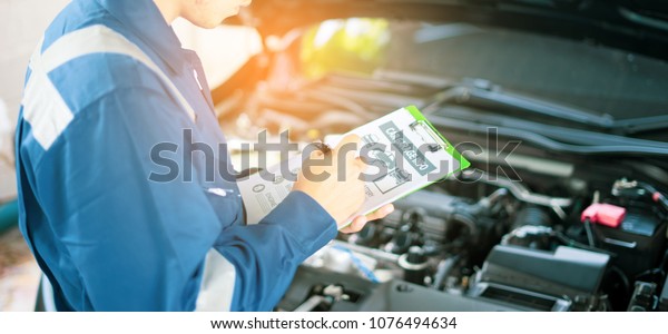 car service, repair, maintenance  concept - Asian\
auto mechanic man or Smith writing to the clipboard at workshop or\
warehouse, technician doing the checklist for repair machine a car\
in the garage