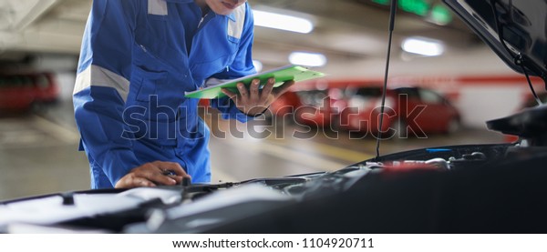 car service, repair, maintenance concept -\
Asian auto mechanic man or Smith writing to the clipboard at\
workshop warehouse, technician doing the checklist for repair\
machine a car in the\
garage,banner