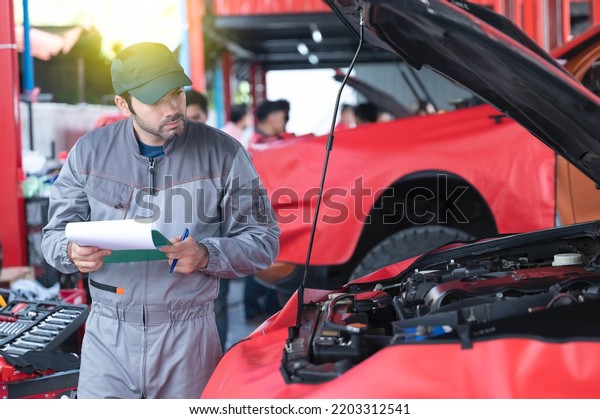 car service, repair, maintenance concept - Arab\
auto mechanic man or Smith writing to the clipboard at workshop\
warehouse, technician doing the checklist for repair machine a car\
in the garage