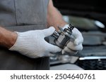 Car service. Repair and maintenance of a passenger car. An auto mechanic holds a new high-pressure fuel pump in his hands. Checking the serviceability of the spare part before installation.