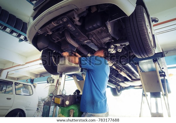 Car\
service, repair & maintenance. Professional car mechanic man\
working under lifted car in auto repair\
service.