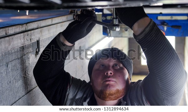 Car service. Thick mechanic man standing in\
inspection pit and working with a\
wrench