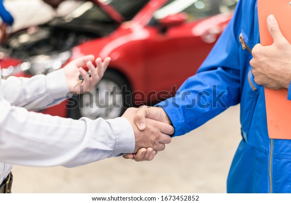 Car service,\
vehicle repair concept : Car service technician shaking hands with\
vehicle owner customer after sending car for repairing or check at\
automobile service center.
