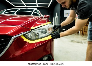 Car service worker applying protective tape on the car details before polishing. - Shutterstock ID 1831366327