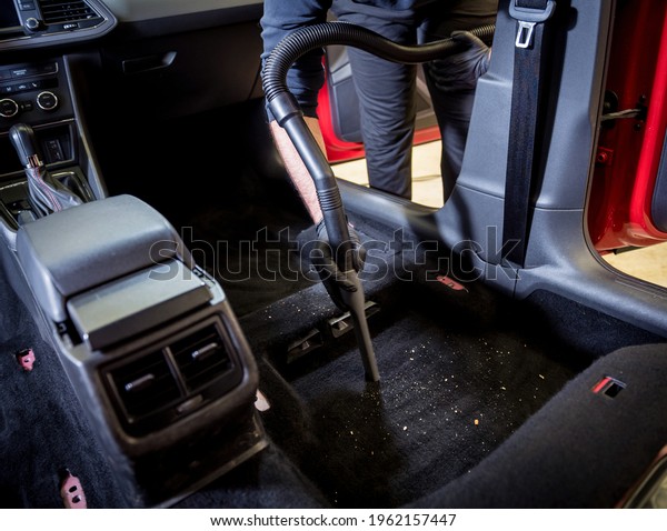 Car service worker cleaning car interior with a\
vacuum cleaner