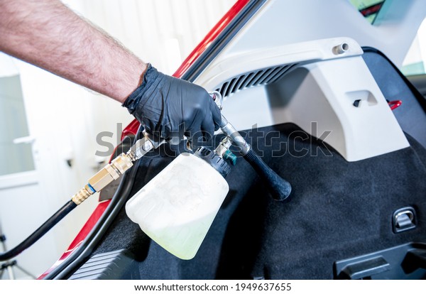 A car service worker cleans interiror with a\
special foam generator