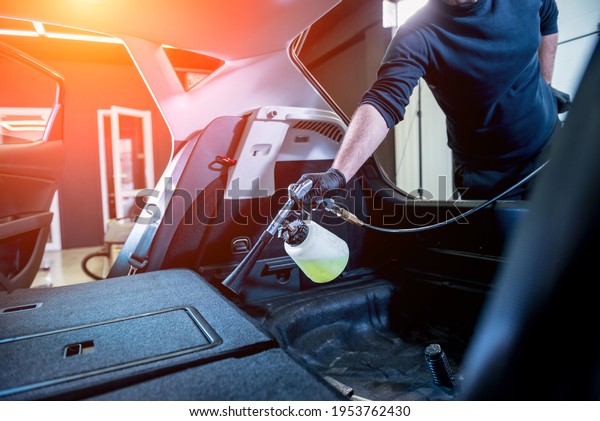 A car service worker cleans interiror with a\
special foam generator