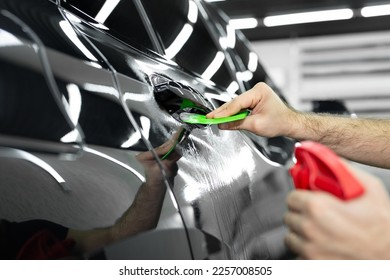Car service worker glues an anti-gravity film on the car body with a scraper in a car detailing workshop. - Shutterstock ID 2257008505