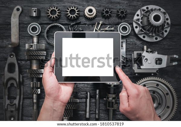 Car service worker is holding a blank screen\
digital tablet above spare parts background. Car spare parts order\
online concept.