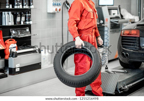 Car service worker in red\
uniform carrying new tires at the tire mounting service or\
shop