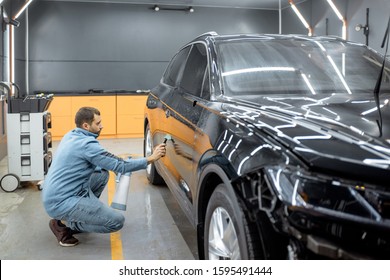 Car service worker removing water from the car body with a scraper, before anti-gravel film apply at the vehicle detailing service