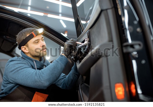 Car service worker in uniform provides a\
professional vehicle interior cleaning, wiping door panel with a\
brush at the car service\
station