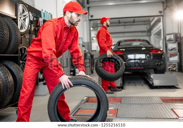Car service workers in red\
uniform carrying new tires at the tire mounting service or\
shop