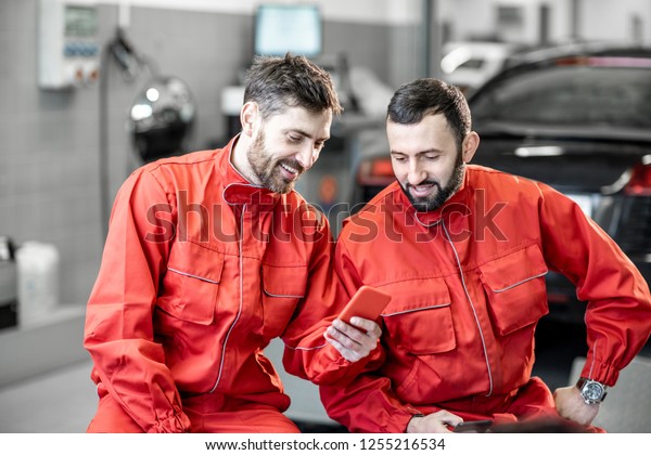Car\
service workers in red uniform having a break sitting together with\
phone on the wheels at the tire mounting\
service