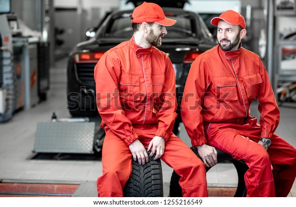Car service\
workers in red uniform having a break sitting together on the\
wheels at the tire mounting\
service