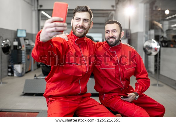 Car service\
workers in red uniform making selfie photo with phone during a\
break at the tire mounting\
service