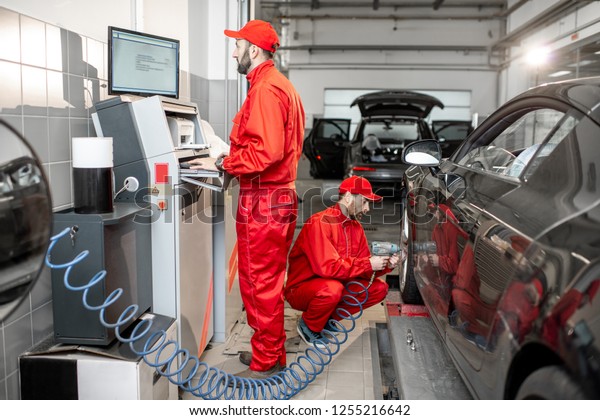 Car service\
workers in red uniform balancing and changing wheels of a sport car\
at the tire mounting\
service