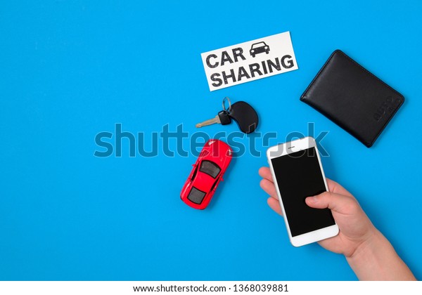 Car sharing\
app concept. Toy car, car key, auto drive license, human hand with\
smartphone and text sign \