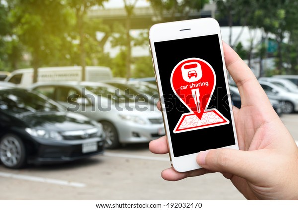 Car\
sharing service or rental concept. Sharing economy and\
collaborative consumption. Customer hand holding smart phone with\
icons application screen and blur cars\
background.