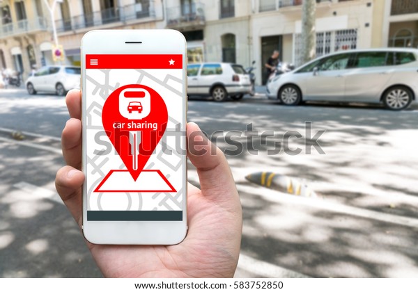 Car\
sharing service or rental concept. Sharing economy and\
collaborative consumption. Customer hand holding smart phone with\
icons application screen and blur car\
background.