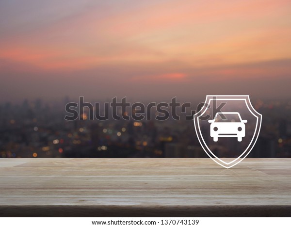Car with shield flat icon on wooden table over\
blur of cityscape on warm light sundown, Business automobile\
insurance concept