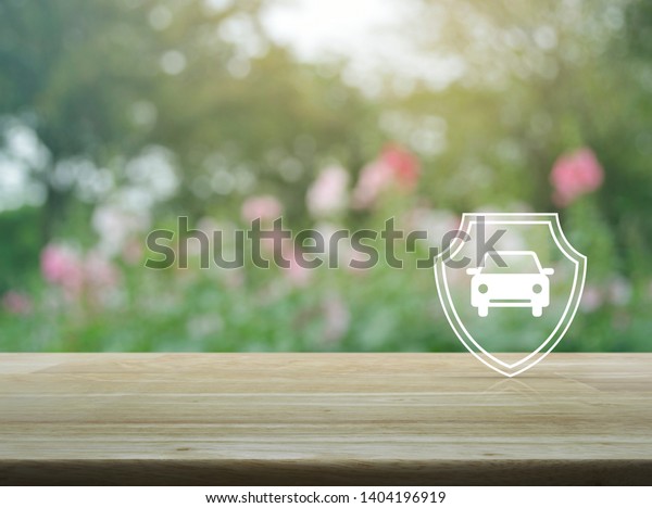 Car\
with shield flat icon on wooden table over blur pink flower and\
tree in garden, Business automobile insurance\
concept