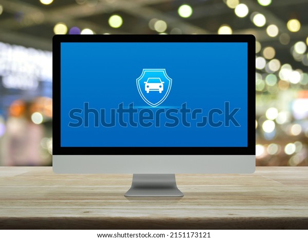 Car with shield flat\
icon on desktop modern computer monitor screen on wooden table over\
blur light and shadow of shopping mall, Business automobile\
insurance online concept