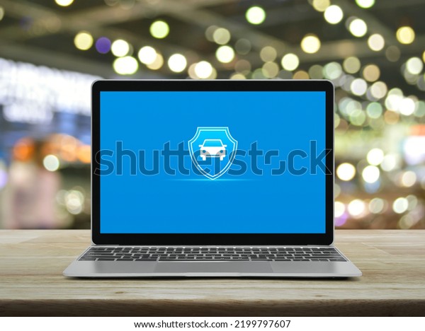 Car with shield flat\
icon on modern laptop computer monitor screen on wooden table over\
blur light and shadow of shopping mall, Business automobile\
insurance online concept