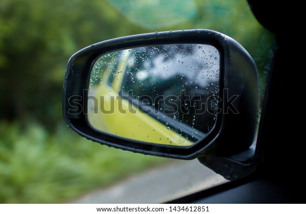 Car side mirror glass with water\
droplets from rain - driver\'s side rear view on rainy\
day