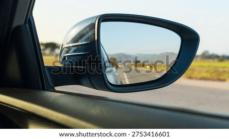 Car side mirror reflecting empty highway and mountain landscape during road trip.