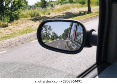 Car side mirror reflects an empty rural road on a sunny day. Travel safety and driving perspective background for road trip transport journey and quiet countryside transportation themes.