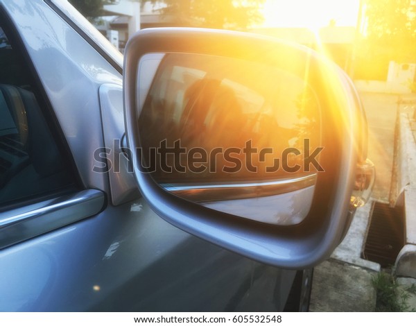 Car side mirror with sun light flaring during sun\
rising on the road
