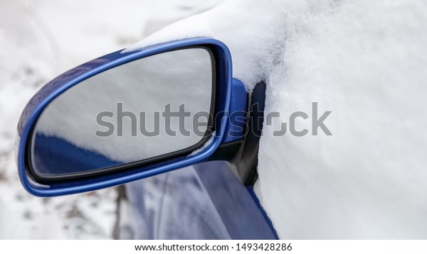 Car side with side rear-view mirror\
completely covered with fluffy snow after\
snowfall
